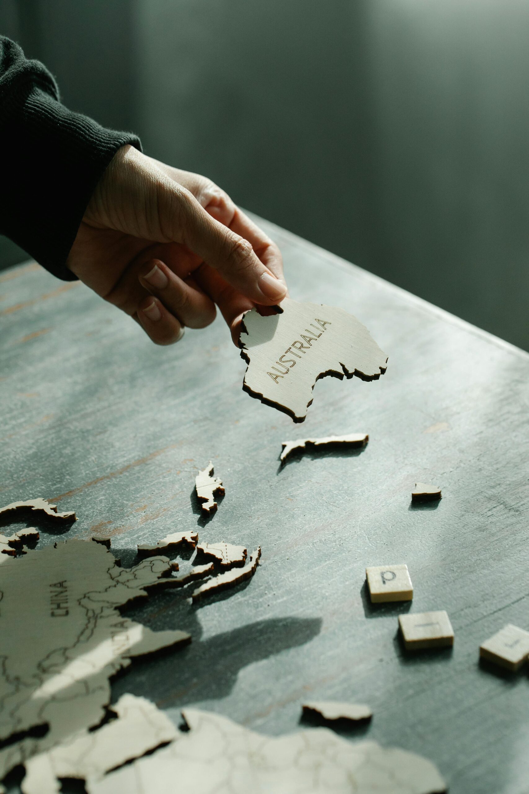 A person places the Australia piece on a wooden world map puzzle, symbolizing connection and exploration.